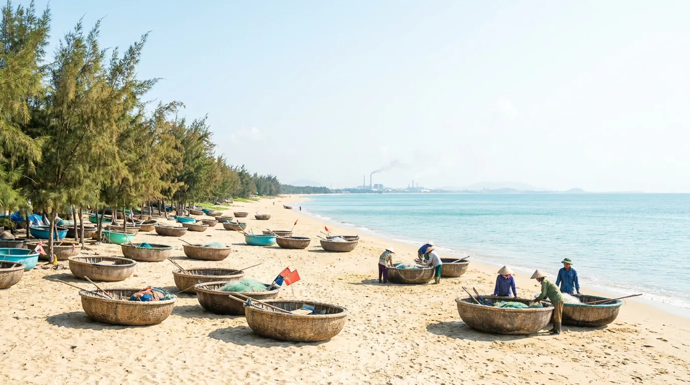 Bãi biển và làng chài ven biển Hà Tĩnh với thuyền thúng, hàng phi lao và cụm công nghiệp mờ phía xa trong nắng sớm — ảnh minh họa