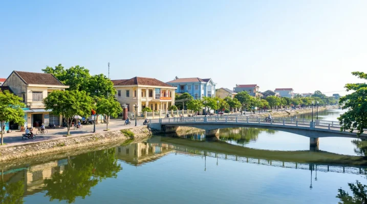 Khu trung tâm đô thị ven sông ở Hà Tĩnh với phố xá, cầu và cây xanh hai bên bờ trong nắng sớm — ảnh minh họa
