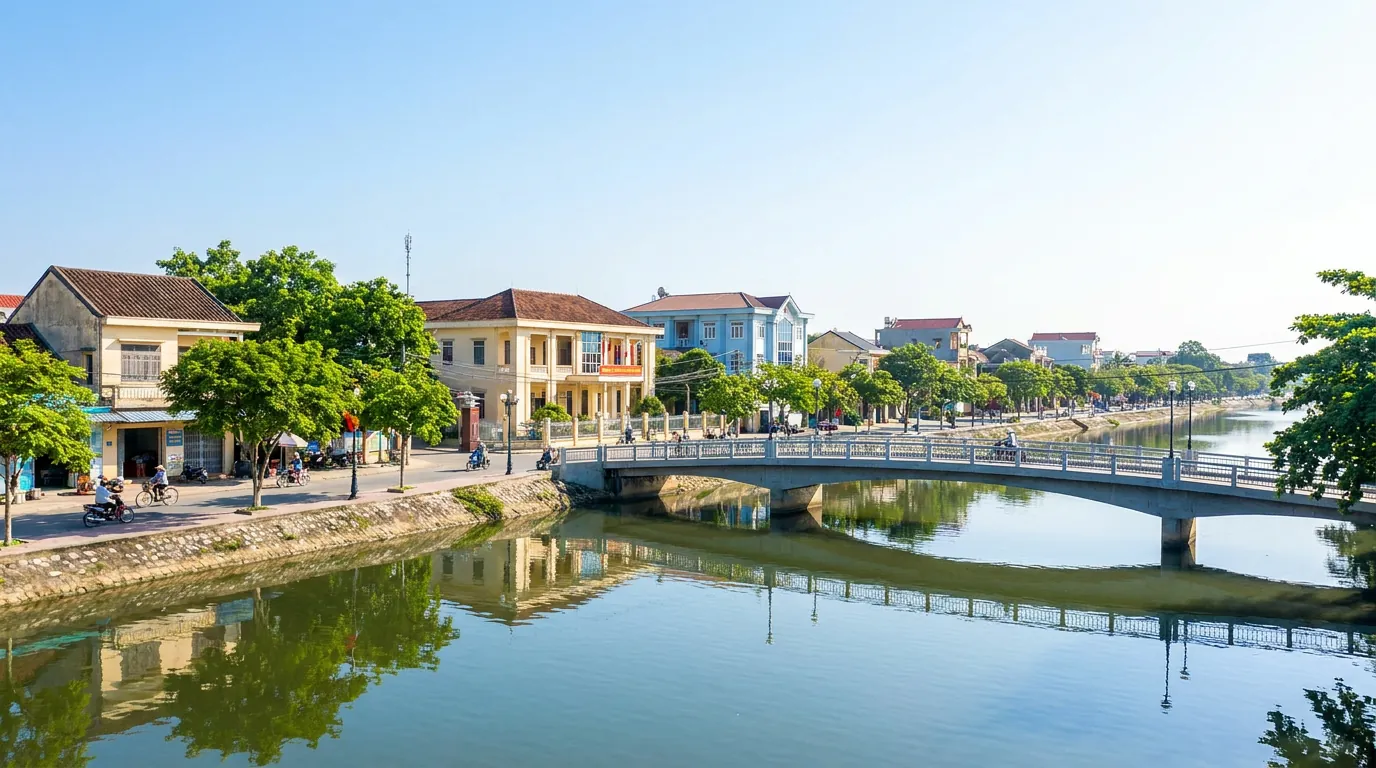 Khu trung tâm đô thị ven sông ở Hà Tĩnh với phố xá, cầu và cây xanh hai bên bờ trong nắng sớm — ảnh minh họa